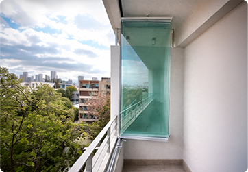 Balcony with a glass windscreen and metal railing, overlooking trees and a distant city skyline.
